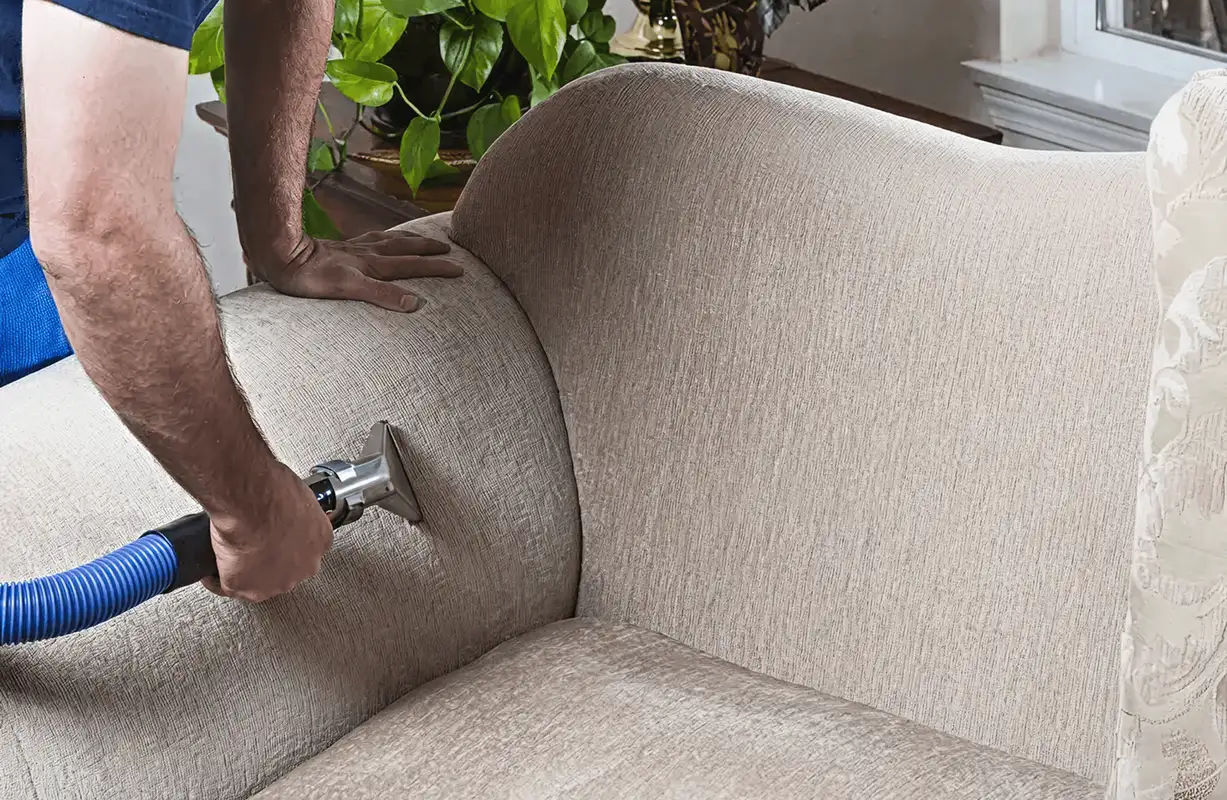 Professional upholstery cleaner deep-cleaning a fabric sofa with a handheld extraction tool and hose, Sacramento, CA.